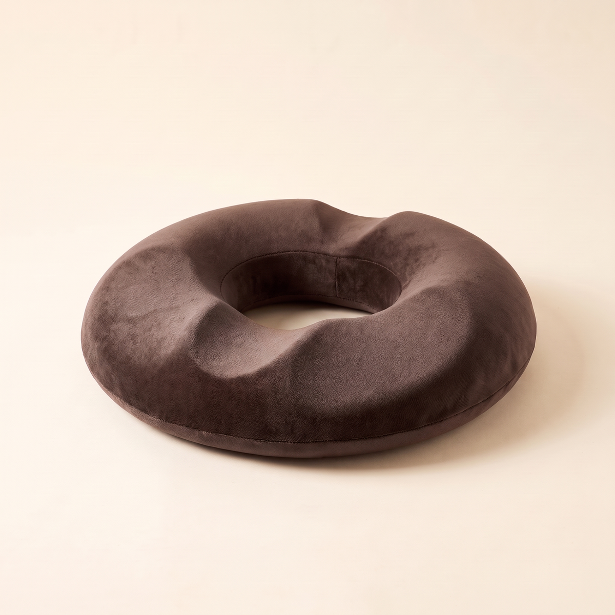Memory foam donut seat cushion in brown on a cream studio background