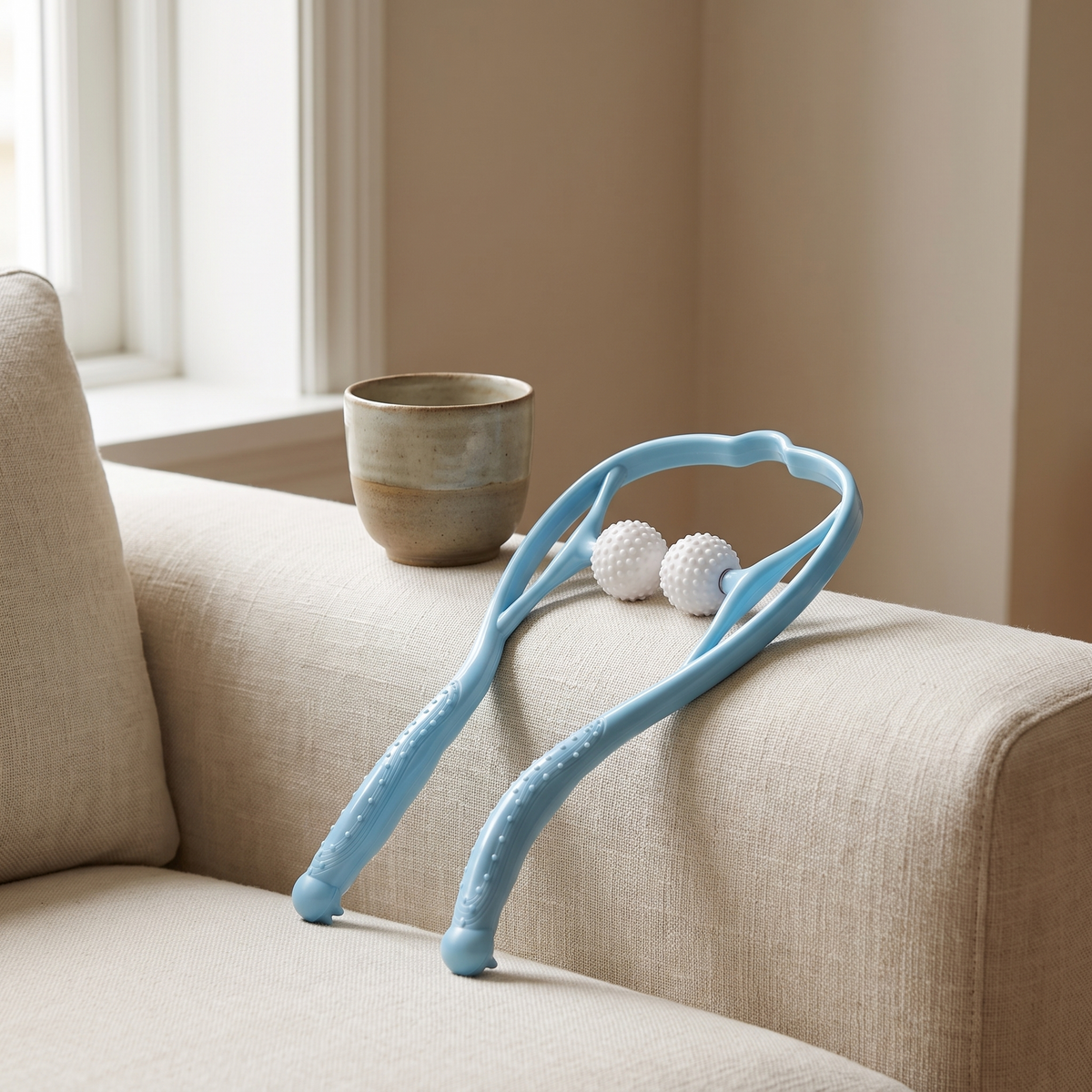 Dual point neck massager resting on the arm of a cream linen sofa beside a ceramic cup