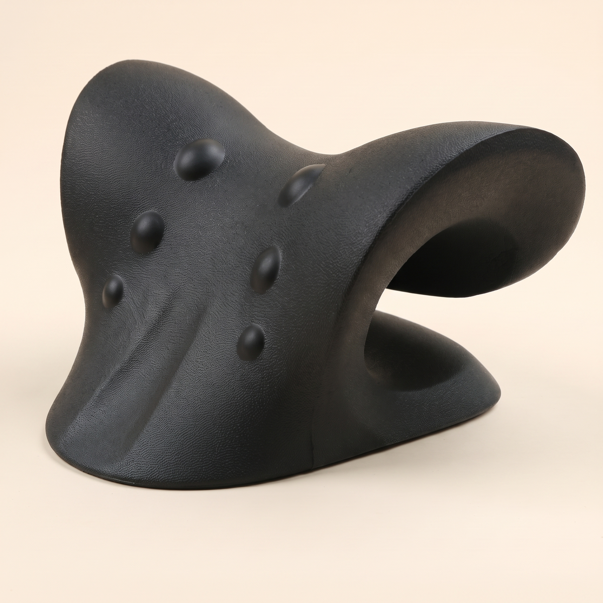 Black C shaped cervical traction pillow on a cream studio background