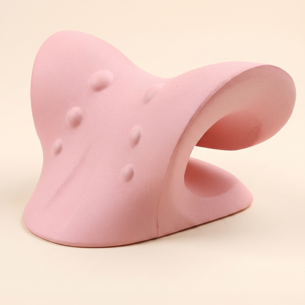 Pink C shaped cervical traction pillow on a cream studio background