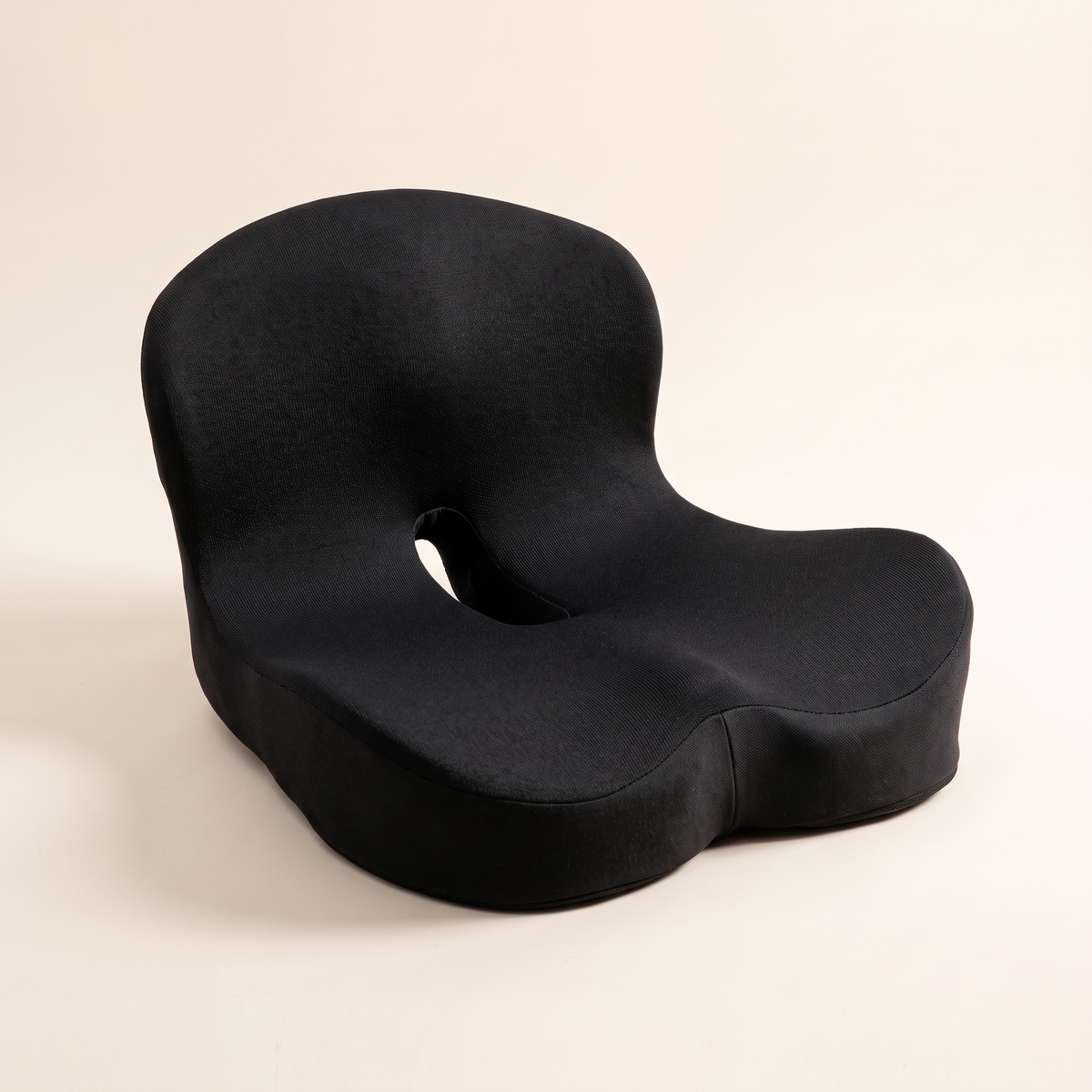 Ergonomic memory foam seat cushion in black knit on a cream studio background
